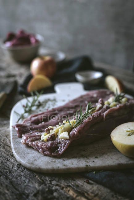 Mela tagliata e rosmarino fresco su fetta di carne cruda su tavolo di legno — Foto stock