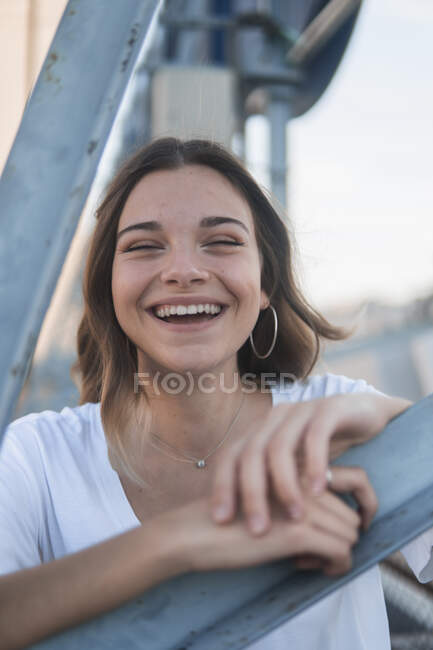 Wunderbare junge Frau steht hinter Metallkonstruktion auf der Straße und lacht in die Kamera — Stockfoto