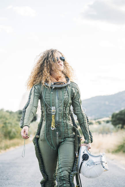 Female astronaut with curly hair walking along road in nature — Stock Photo