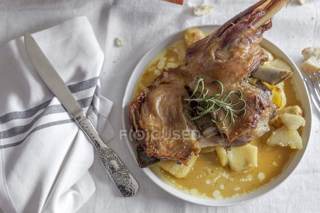Cordeiro assado com batatas servidas em prato em toalha de mesa branca — Fotografia de Stock