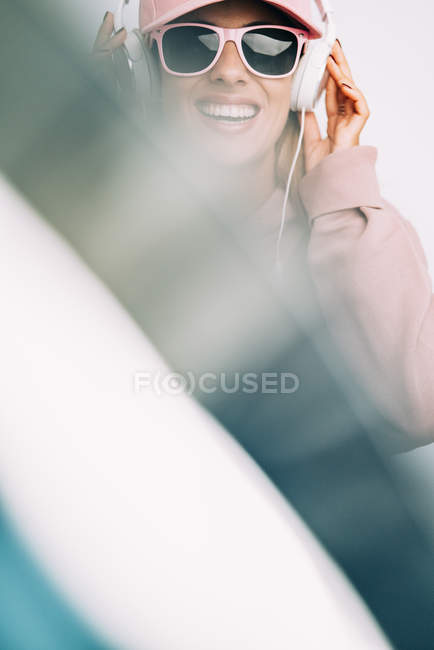Femme en tenue rose et lunettes de soleil écoutant de la musique sur fond flou — Photo de stock