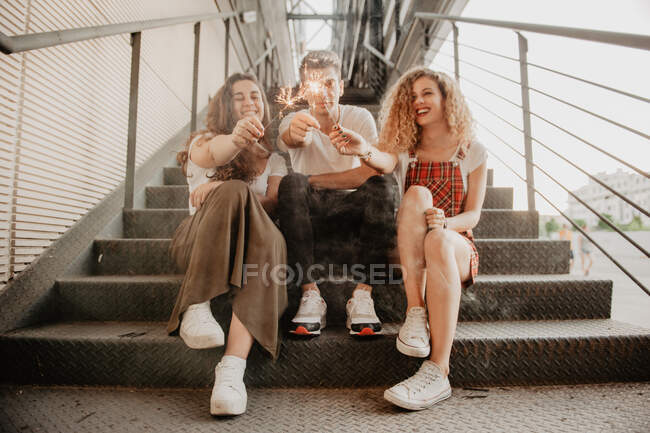 Drei gut gelaunte Freunde lachen und brennen, während sie auf Metalltreppen auf der Stadtstraße sitzen — Stockfoto
