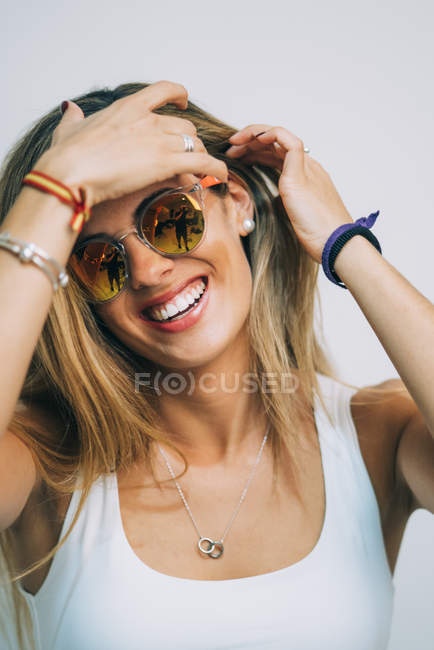 Junge blonde Frau in weißem Top und Sonnenbrille stehend und Haare auf weißem Hintergrund berühren — Stockfoto