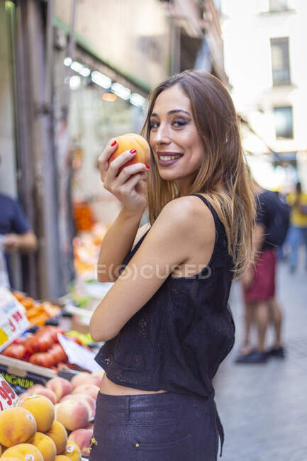 Mujer alegre mordiendo melocotón en el mercado - foto de stock