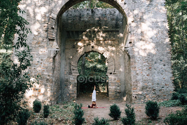 Woman doing yoga under old crumbling arch — Stock Photo