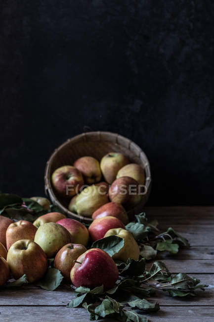 Mele fresche mature e foglie con cesto su tavola rustica in legno — Foto stock