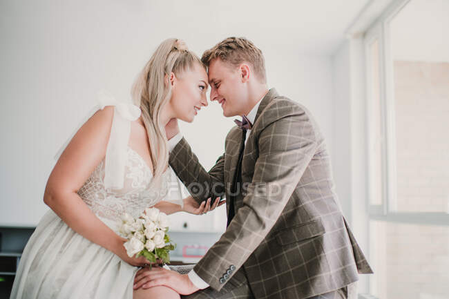 Vista lateral de la feliz pareja casada abrazándose y mirándose en casa - foto de stock