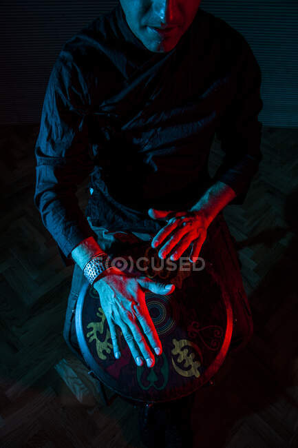 Молодий ударник, який практикує техніку з тамаром або барабаном, кольорове освітлення в червоному і синьому. рук дивитися — стокове фото