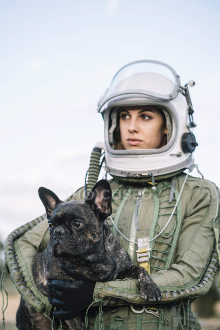 Sonriente chica usando casco de espacio viejo y traje espacial celebración de perro en la naturaleza - foto de stock