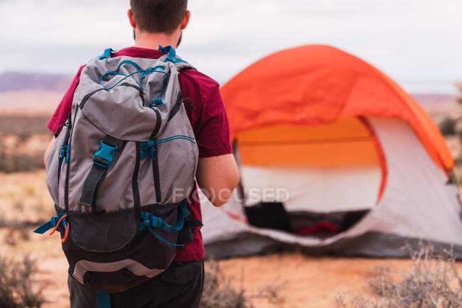 Vue arrière de l'homme avec sac à dos marchant vers la tente moderne tout en campant dans le désert — Photo de stock