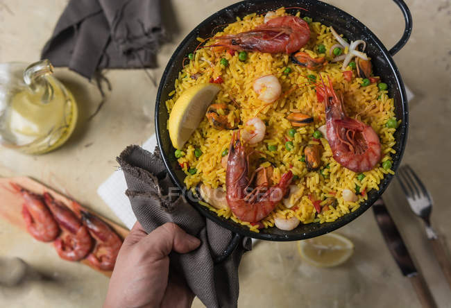 Человеческая рука держит кастрюлю традиционной испанской паэльи маринера с рисом, креветками, кальмарами и мидиями — стоковое фото