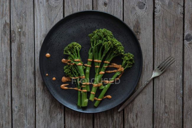 Брокколи с соусом ромеско на черной тарелке с вилкой на деревянном столе — стоковое фото