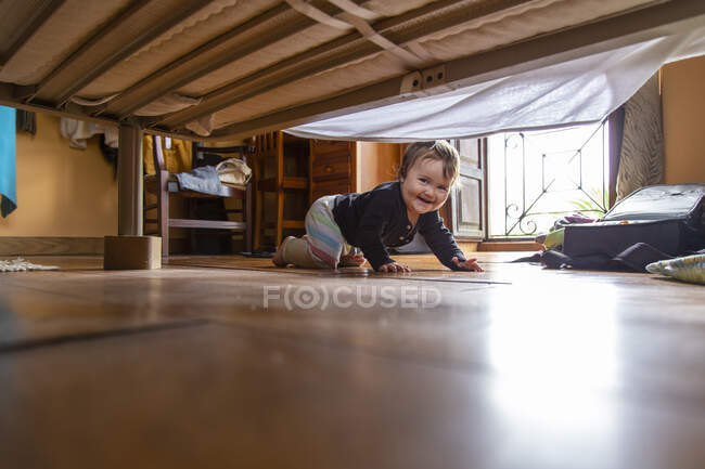 Vista de debaixo da cama de criança adorável rindo no chão olhando para a câmera — Fotografia de Stock
