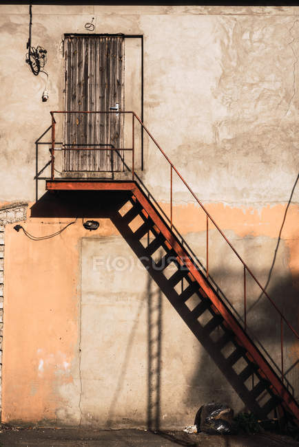 Gradini in metallo e porta in legno situato su muro di cemento squallido di costruzione — Foto stock