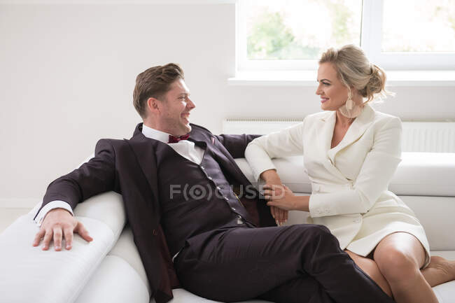 Vista de recém-casados modernos elegantes no interior branco simples no sofá na luz do dia suave — Fotografia de Stock