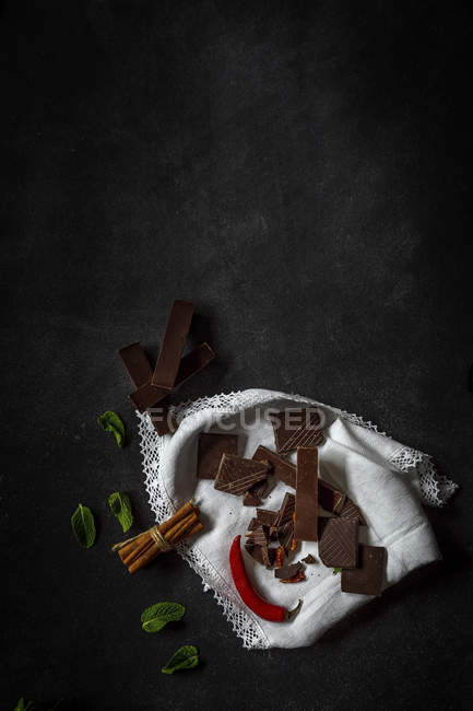 Chocolate pieces with red chilli pepper, mint and cinnamon on dark background — Stock Photo