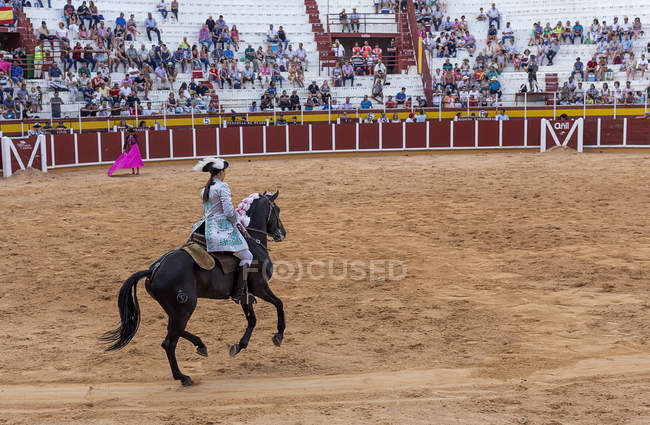 Espanha, Tomelloso - 28. 08. 2018. Vista de fêmea toureiro equitação cavalo na área arenosa com pessoas na tribuna — Fotografia de Stock