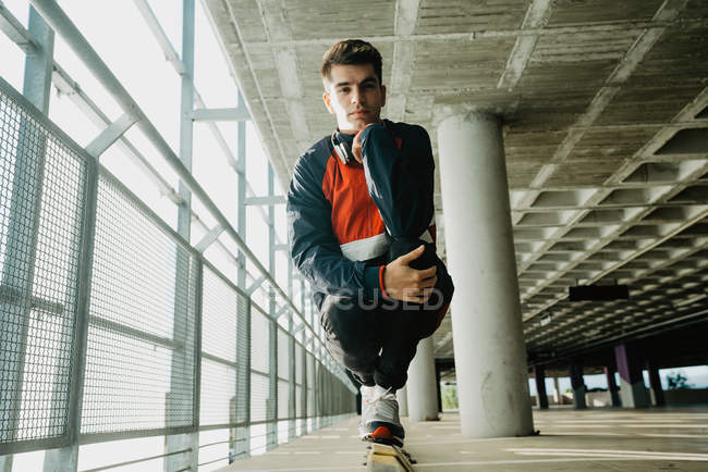 Retrato de un joven en ropa deportiva de pie sobre raíl en el edificio con pilares - foto de stock