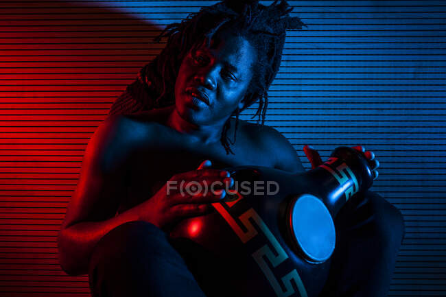 Joven rastafari africano hombre disfruta ensayando y juega udu, iluminación de color rojo y azul - foto de stock