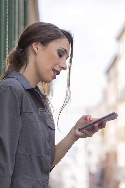 Mujer usando teléfono inteligente cerca del edificio en la calle - foto de stock