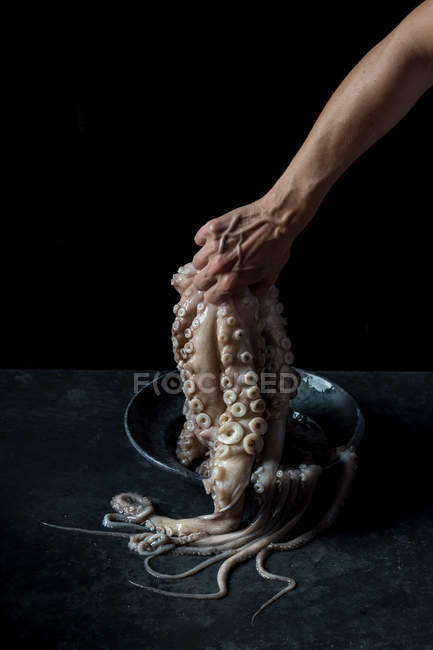 Human hand holding octopus over plate on black marble background — Stock Photo