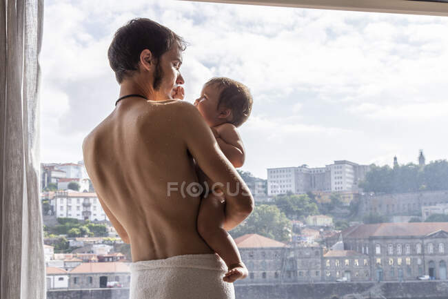 Hombre con bebé cerca de la ventana a la luz del sol - foto de stock