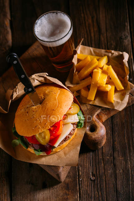 Вкусный гамбургер для гурманов с ножом на деревянной доске с пивом и картошкой фри — стоковое фото