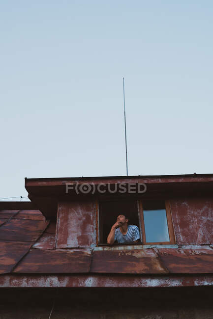 De baixo tiro de macho olhando para fora janela de cabana resistida em pequeno assentamento na Bulgária, Balcãs — Fotografia de Stock