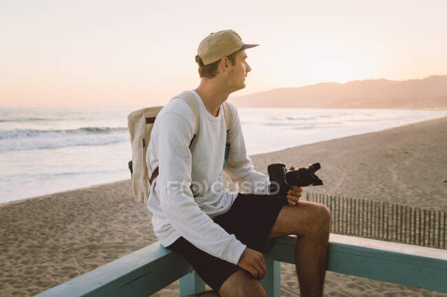 Homme avec appareil photo assis sur la plage — Photo de stock