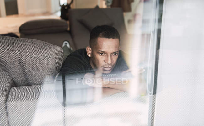 Träumender schwarzer Mann lehnt sich an die Hände, während er auf der Couch sitzt und wegschaut — Stockfoto