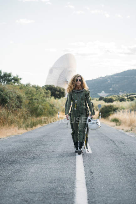 Astronauta feminina com cabelo encaracolado andando ao longo da estrada na natureza — Fotografia de Stock