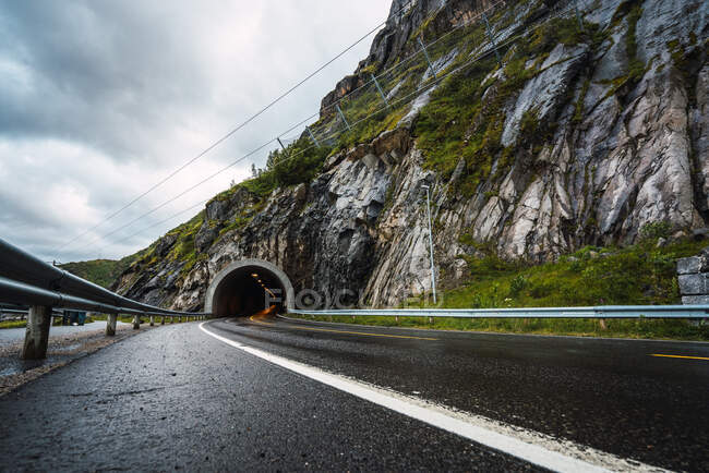 Empty asphalt motorway covered with raindrops leading to tunnel in rocky hill on background of overcast sky — Stock Photo