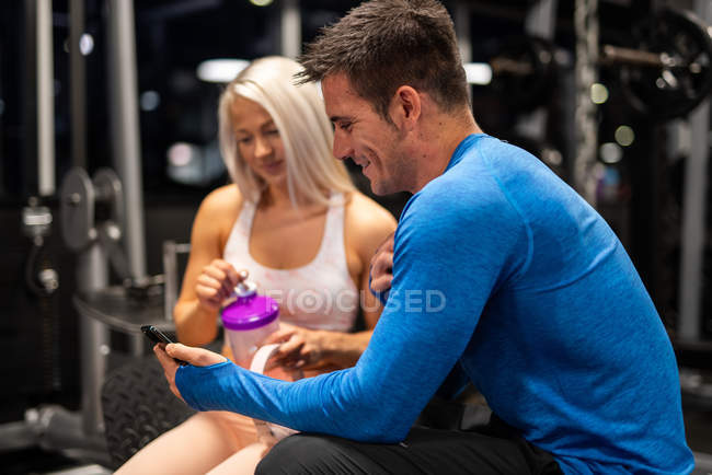 Спортсмен і жінка, використовуючи смартфон у спортзалі — стокове фото