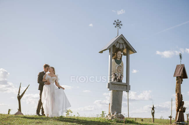 Jeune couple nouvellement marié debout au monument et embrassant — Photo de stock