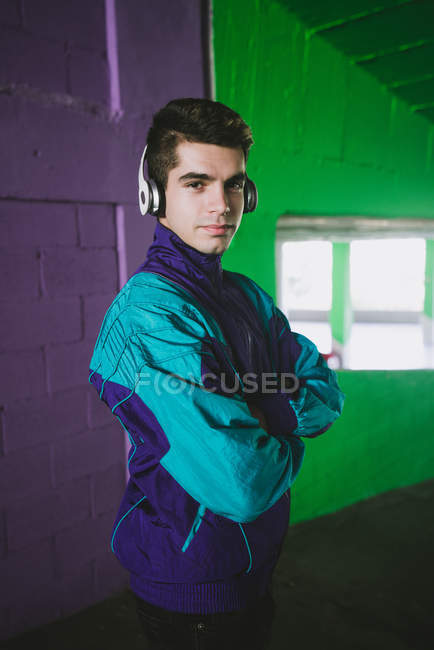 Sonriente joven en ropa deportiva escuchando música con auriculares contra la pared colorida - foto de stock