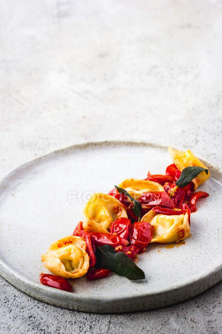 Leckeres Gericht von Tortellini mit Tomaten auf Teller auf grauer Tischplatte serviert — Stockfoto