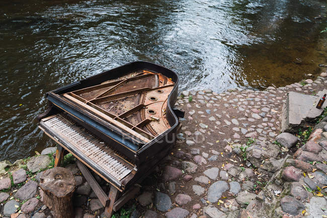 Piano viejo roto en el pavimento cerca del lago - foto de stock