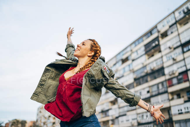Рыжая молодая женщина с распростертыми руками стоит напротив жилого дома — стоковое фото
