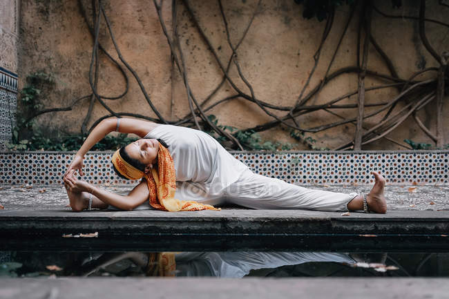 Женщина, сидящая в позе йоги возле бассейна в старом саду — стоковое фото