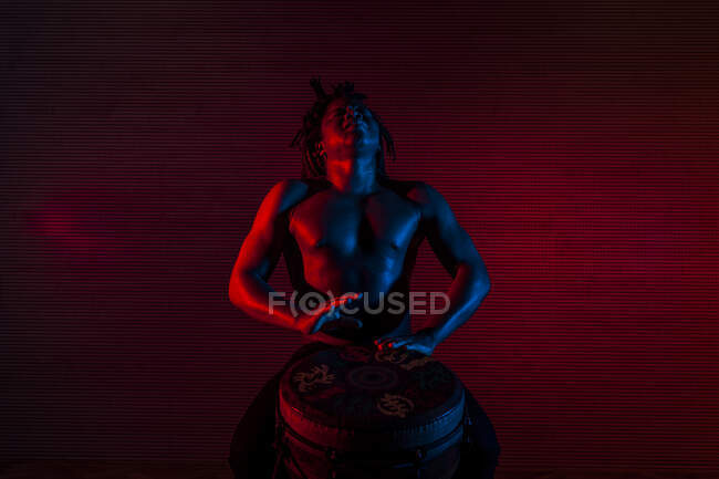 Jeune homme rastafari africain aime répéter et joue tam tam, éclairage coloré rouge et bleu — Photo de stock