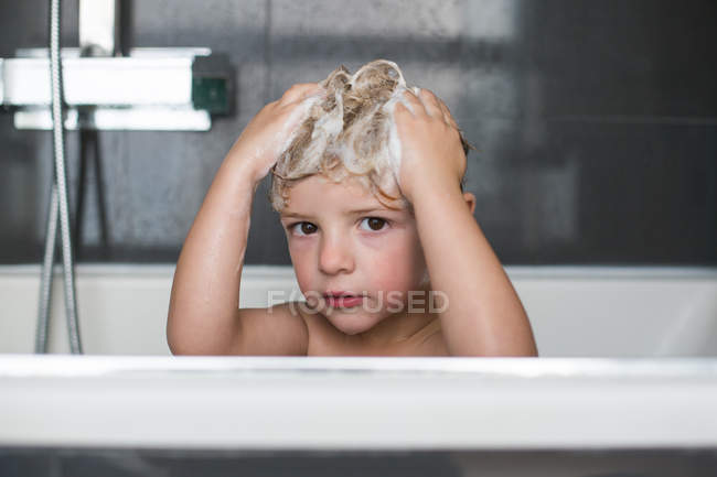 Retrato de niño pequeño con espuma en el pelo sentado en el baño - foto de stock