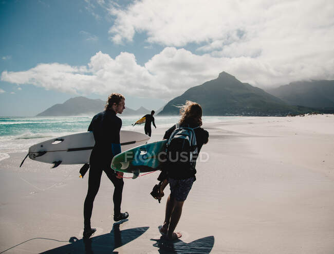 Вид на людей с досками для серфинга, идущих по песчаному берегу у океана. — стоковое фото