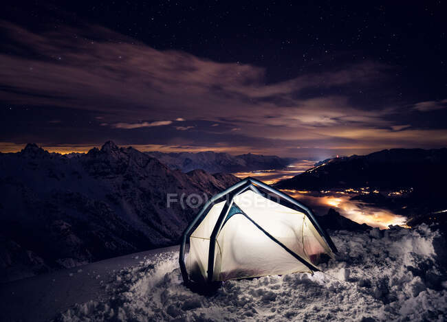 Tenda con luce accesa in montagna coperta di neve di notte. — Foto stock