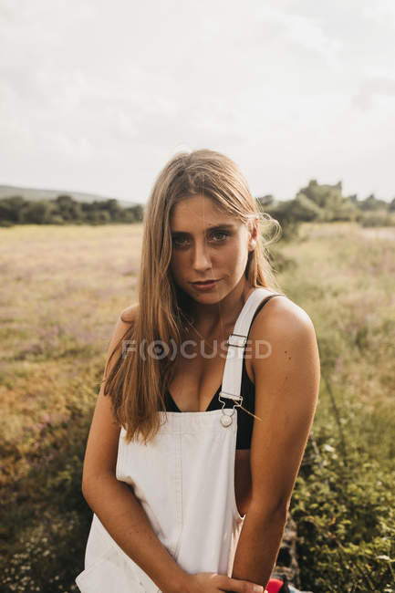 Schöne braun gebrannte blonde Frau trägt schwarzen BH mit weißem Overall und posiert zärtlich vor der Kamera auf dem Land — Stockfoto