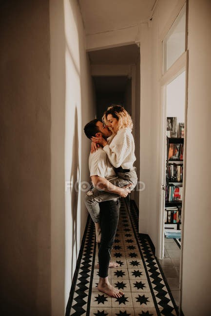 Homem apaixonado e mulher abraçando e beijando na parede no salão em casa — Fotografia de Stock