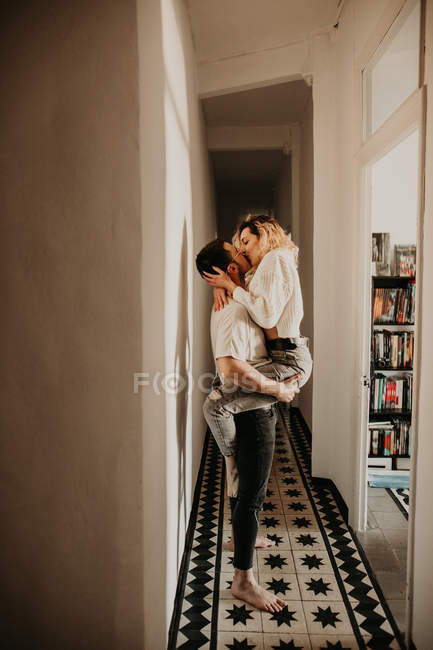 Apasionado hombre y mujer abrazando y besándose en la pared en el pasillo en casa - foto de stock