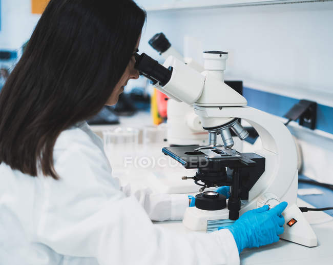 Brunette woman in uniform using microscope in laboratory — Stock Photo
