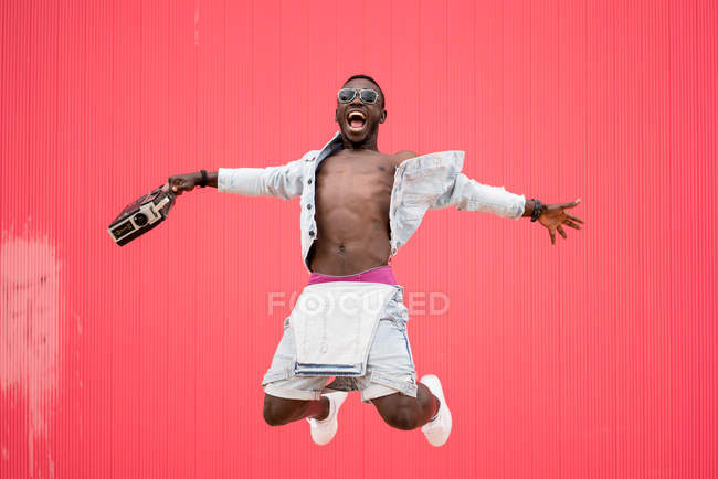 Афроамериканський чоловік стрибає з вінтажним радіопристроєм на червоному тлі — стокове фото