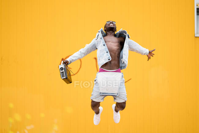 Homme afro-américain sautant avec dispositif de radio vintage sur fond jaune — Photo de stock