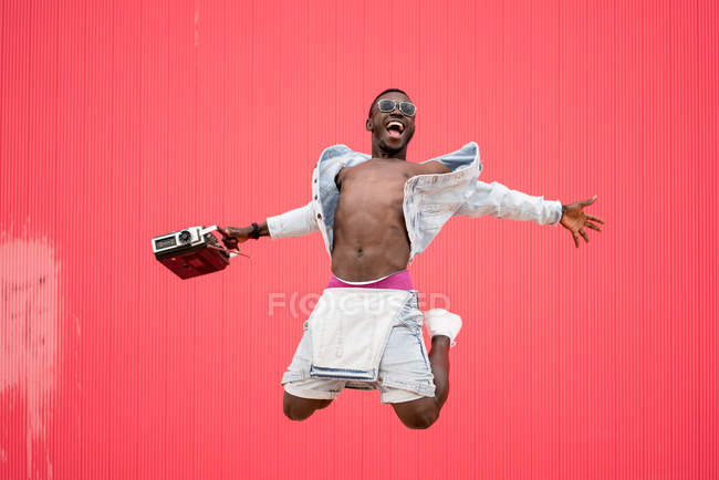 Афроамериканський чоловік стрибає з вінтажним радіопристроєм на червоному тлі — стокове фото